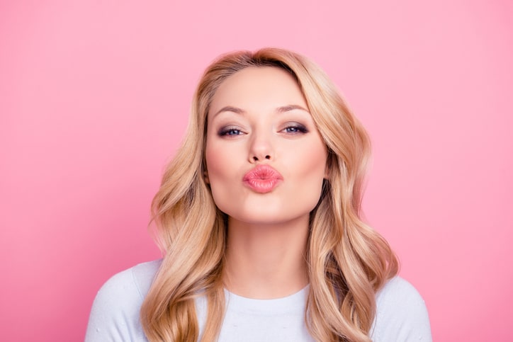 Portrait of cute lovely girl in casual outfit with modern hairdo sending blowing kiss with pout lips looking at camera isolated on pink background. Affection feelings concept