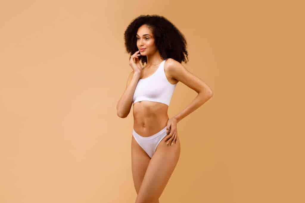 A woman posing in white underwear showing the results of liposuction in Orange County